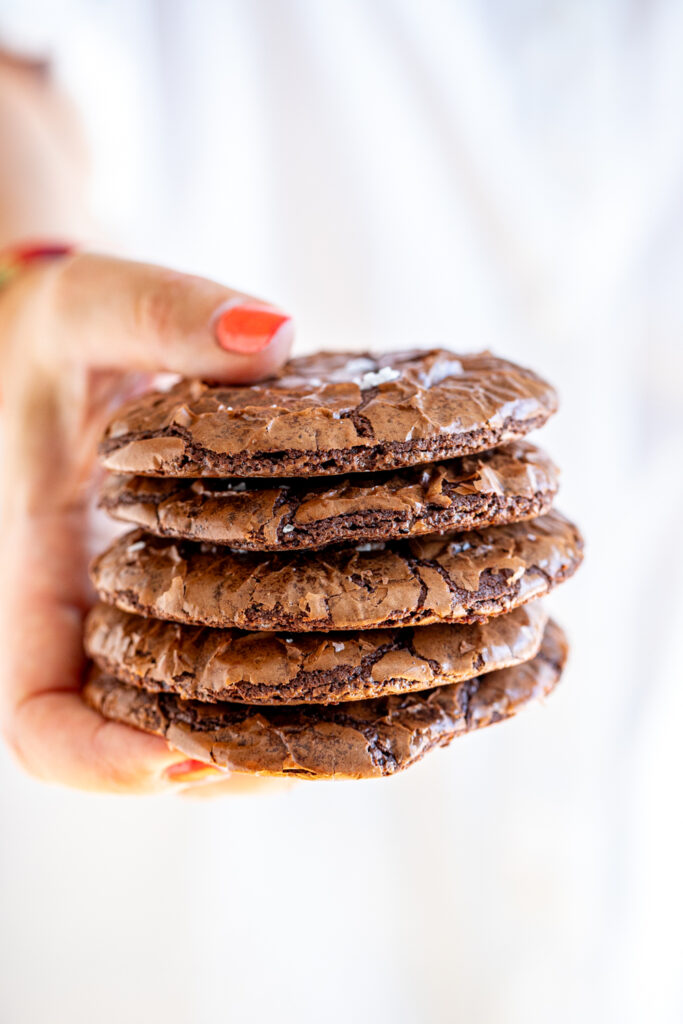 Five chocolate brownie cookies held in a hand with red nail polish.