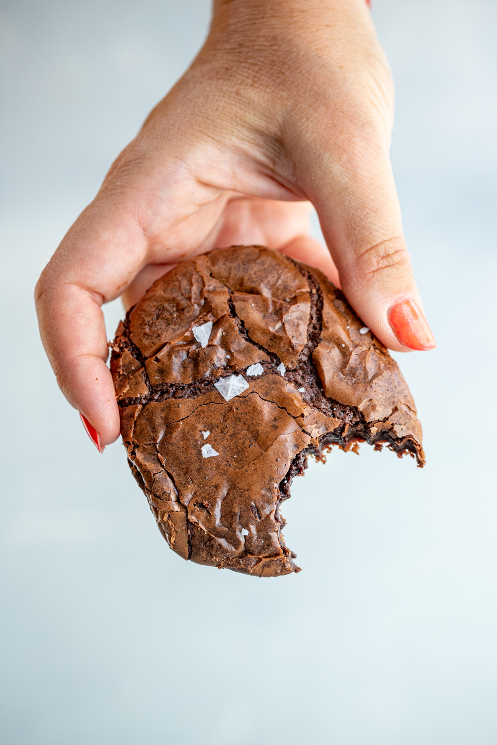 Hand with red nail polish holding a bitten chocolate brownie cookie