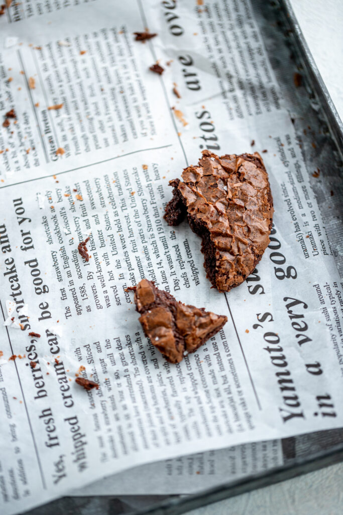 top photo of leftover salty chocolate brownie lying on printed parchment paper, surrounded by crumbs.