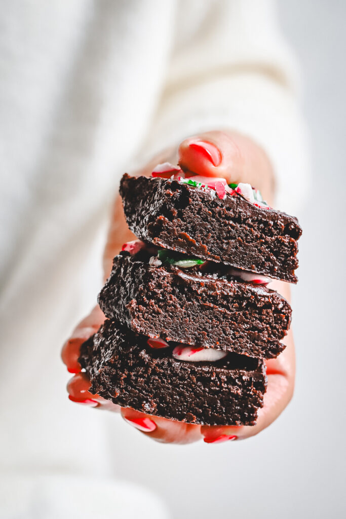 Fudgy Candy Cane Brownies sliced and photographed from the side, showcasing the thick chocolate base, rich ganache layer, and crunchy red, white, and green crushed peppermint candy cane topping. Best Christmas Brownie recipe.