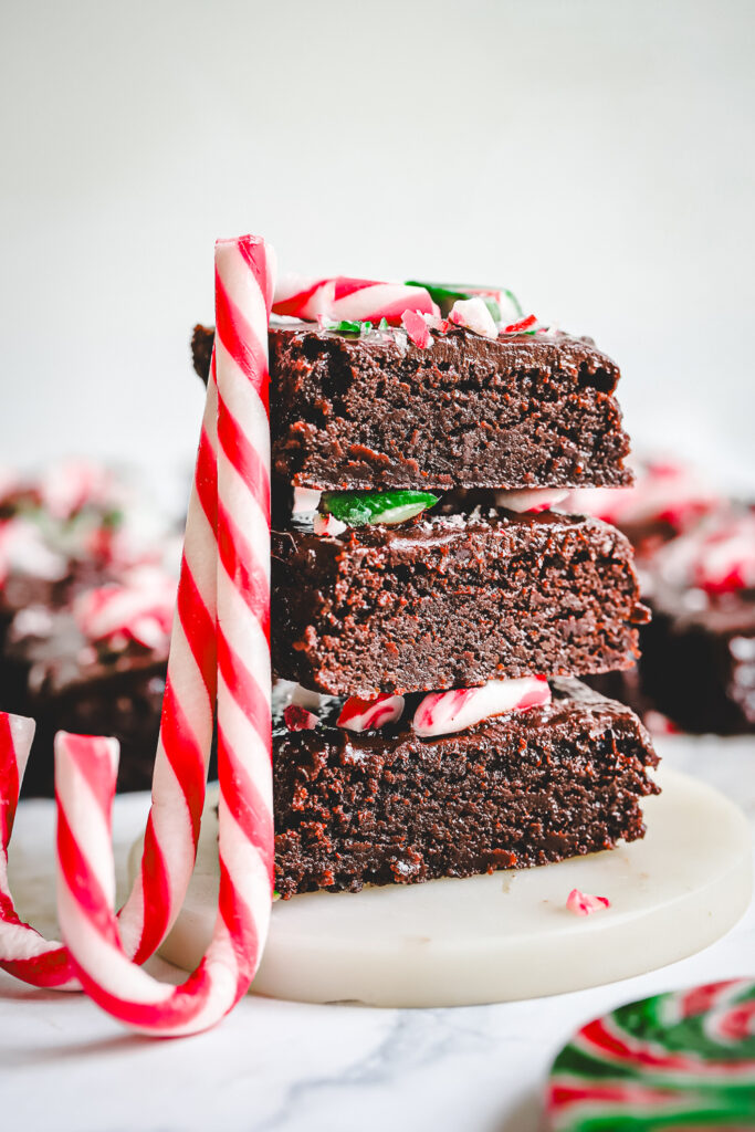 Fudgy Candy Cane Brownies sliced and photographed from the side, showcasing the thick chocolate base, rich ganache layer, and crunchy red, white, and green crushed peppermint candy cane topping. Best Christmas Brownie recipe.
