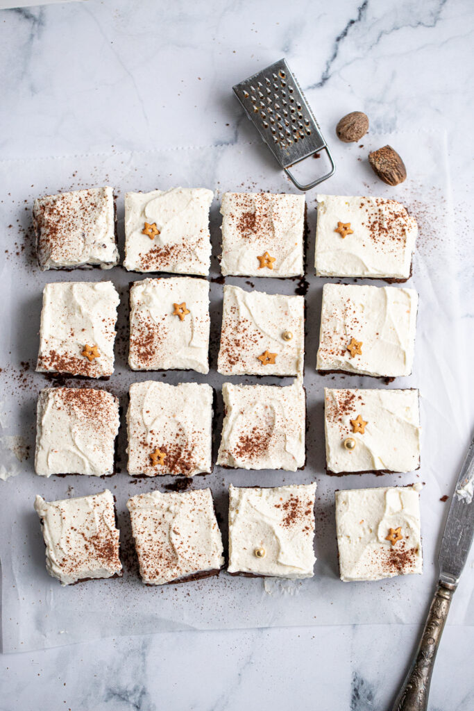 Top-down view of a pan of Gourmet Eggnog Brownies, generously covered in a smooth eggnog cream cheese frosting, sprinkled with fresh nutmeg and sparkling gold sugar stars.