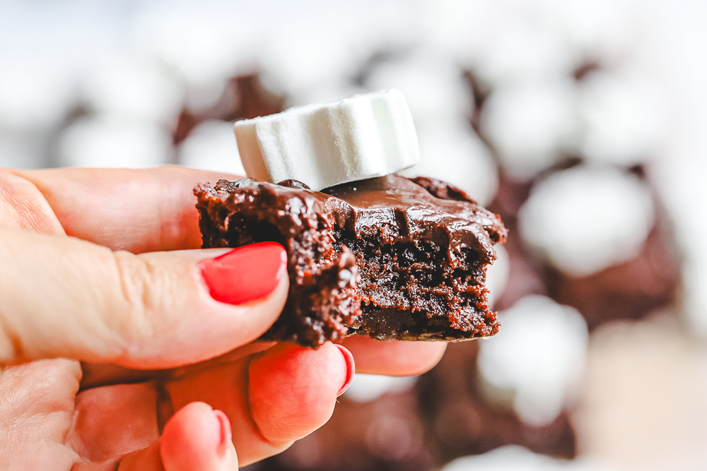 Close-up of a hand holding a gooey hot chocolate brownie slice showing the fudgy, melted chocolate texture.