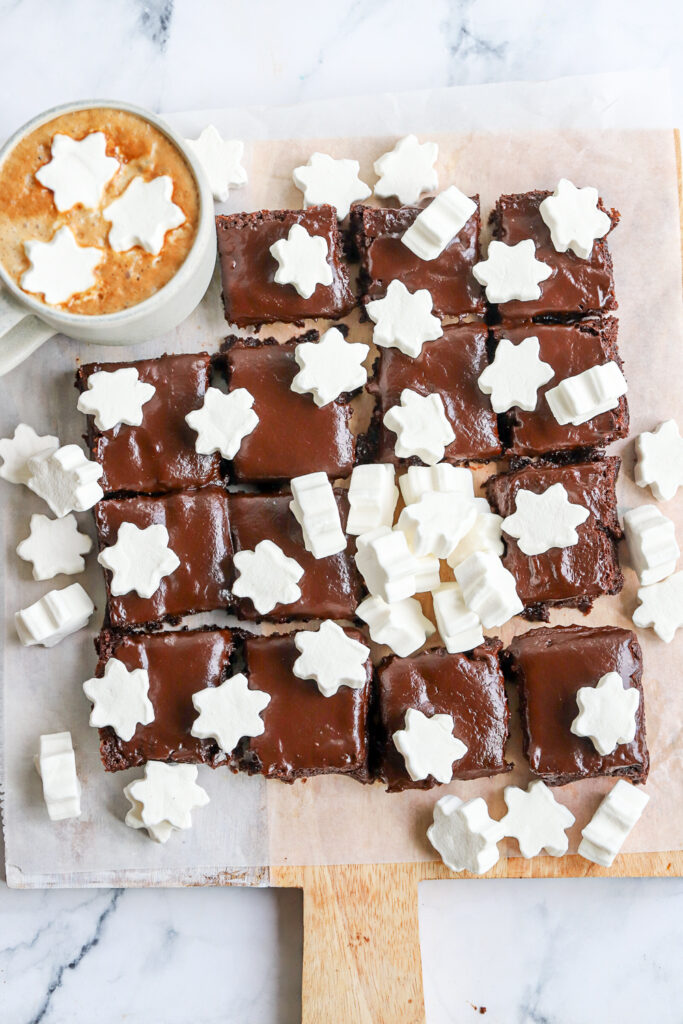 Flat lay photo of fudgy hot chocolate brownies full batch with star marshmallows and a mug of hot cocoa.
