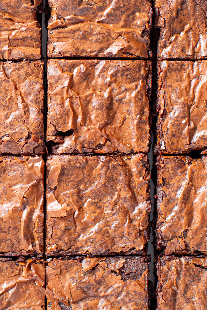 Overhead view of perfectly baked brownies cut into squares, highlighting the shiny, crinkly, crackly top crust.