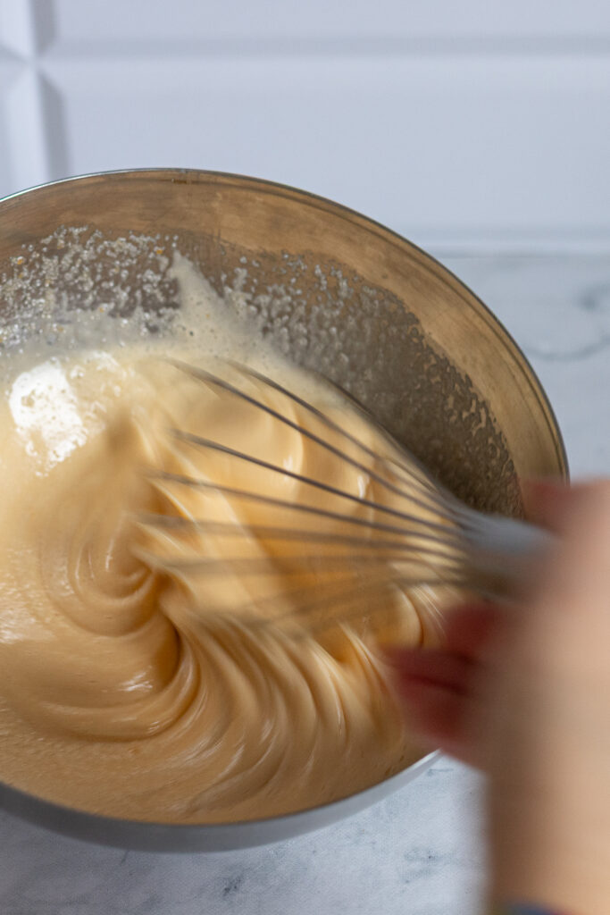 Whisking eggs and sugar vigorously with a hand mixer to achieve the perfect crackly top on brownies.