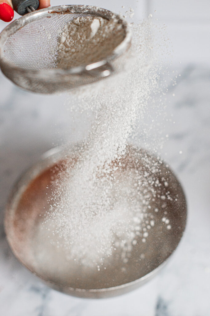 Sifting flour before mixing into the brownie batter to prevent overmixing and ensure a fudgy texture.