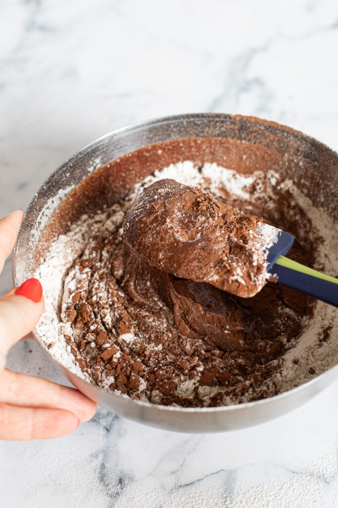Folding sifted flour and cocoa powder into the brownie batter with a spatula to avoid developing gluten and keep the batter fudgy.