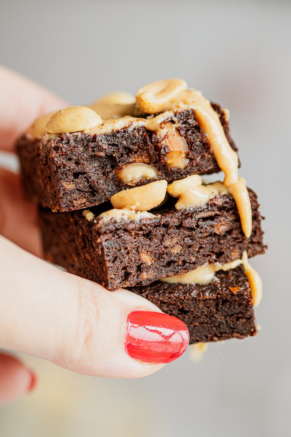 A person holding a stack of healthy flourless sweet potato brownies with melted peanut butter drizzle.