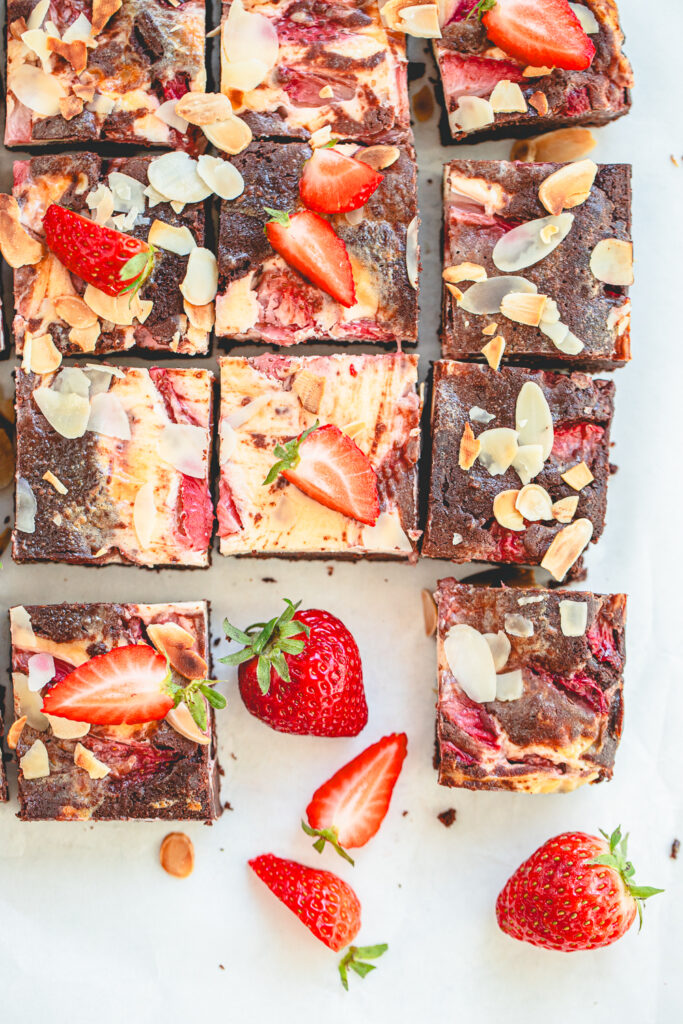 Overhead view (flat lay) of a baking pan filled with strawberry swirl brownies, generously topped with fresh diced strawberries and golden, toasted sliced almonds.