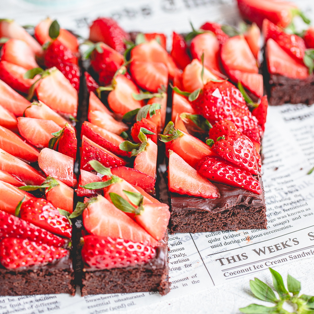Close-up shot of sliced fudgy chocolate brownies showing the dense crumb structure and a layer of chocolate ganache with strawberries.