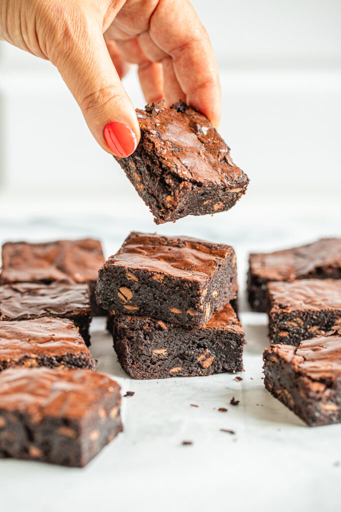 A hand picking up a perfectly cut fudgy brownie square with clean edges from a marble surface